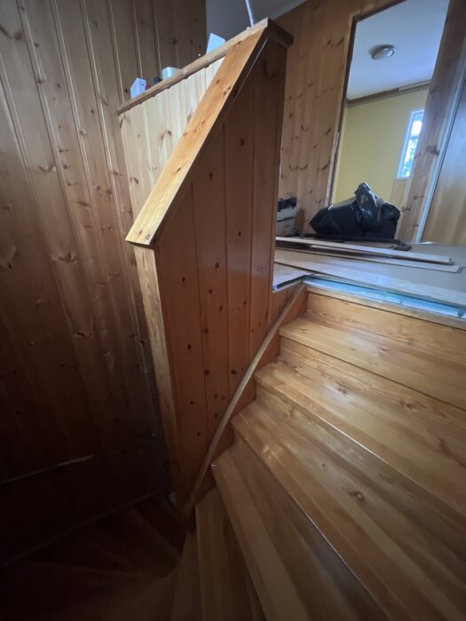 Trätrappa med träpanelräcke i hus. Planer på att byta till smidesräcke. Syns även verktyg och material i bakgrunden.