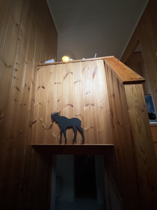 Trappräcke i trä, dekorerat med en silhuett av en älg, i en hemmamiljö med dämpad belysning och brädväggar i trä.