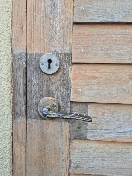 Dörr av trä med gammaldags lås och handtag, delvis slipad, visar olika tränyanser.