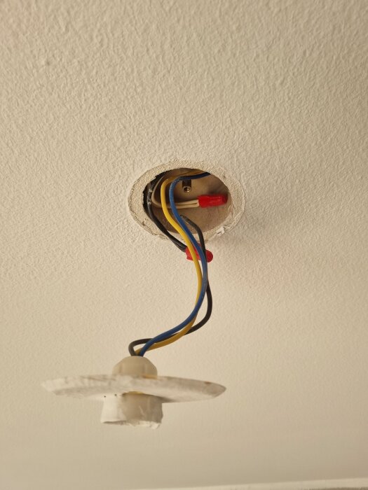 Elektrisk kabelinstallation synlig i ett hål i taket, med flera färgade kablar och en röd skruvplint.