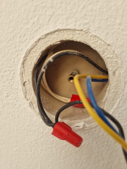 Elektrisk kopplingsdosa med synliga kablar i vägg, några har röda kopplingsmuttrar.