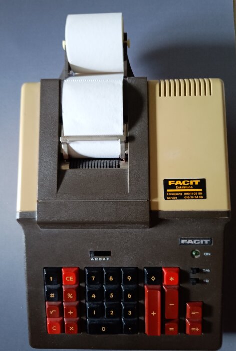 Facit räknemaskin tillverkad i Japan, med kvittorulle, brun och beige design samt röda och svarta knappar, retro stil.