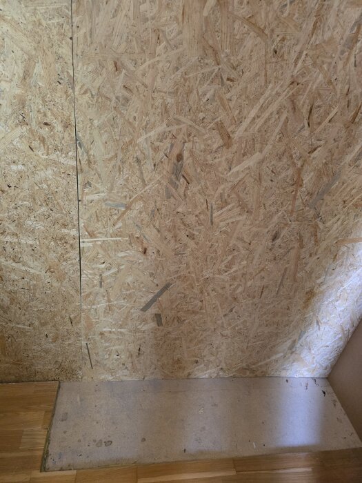 Masonitvägg utan isolering, golv av trä synligt.