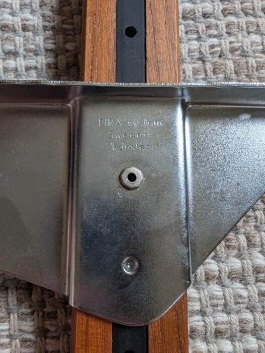 Åttakantig mutter på metallkonsol märkt "PIRA system Sweden Vänster", monterad på träslag med svart metallspår.