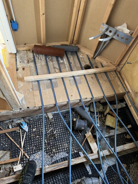 Byggarbetsplats för nytt badrum med synliga vattenrör och golvvärmekablar på öppen bjälklag under ombyggnad.