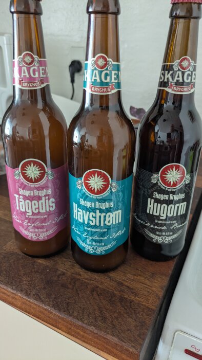 Tre flaskor Skagen Bryghus öl på rad: Tågedis, Havstrøm och Hugorm på en träbänk.