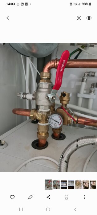 Röd ventil på rörsystem med kopparrör och manometer för luftvattenvärmepump.