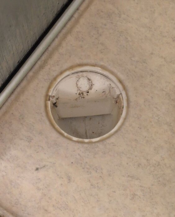 Vattenlås i en duschkabin, utan synlig hasp för enkel borttagning, delvis täckt med smuts eller avlagringar.