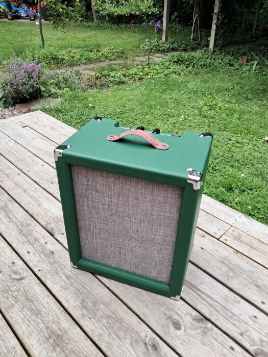 Grön 10" öppen combo-rörförstärkare med älgskinnshandtag, placerad på en träveranda med gräsmatta i bakgrunden.