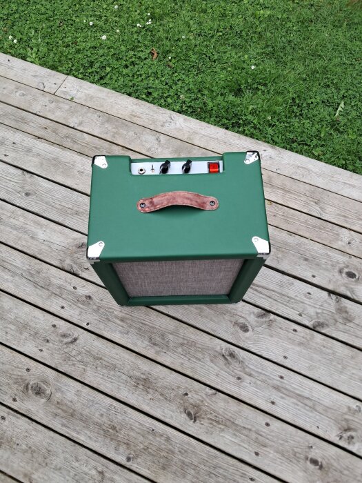 Grön 10" öppen combo-rörförstärkare med älgskinnshandtag, liggande på trädäck med gräsmatta i bakgrunden.