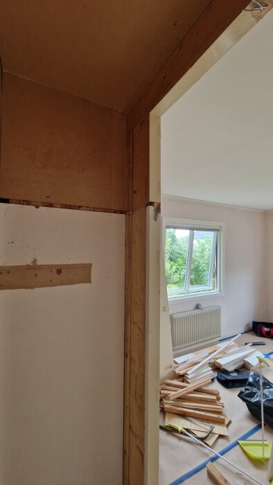 Renovering av garderob med potentiellt bärande brädor, trä och verktyg spridda på golvet, utsikt genom ett fönster i bakgrunden.