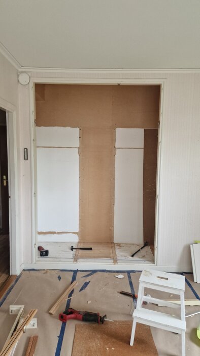 Garderobsrenovering med exponerade brädor, verktyg på golvet och en vit stegpall; fundering om bärande konstruktion i hus från 1949.