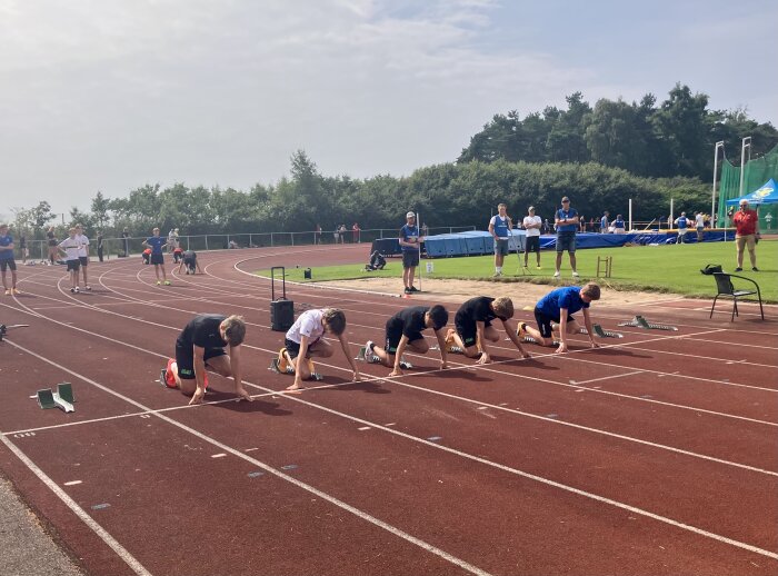 Löpare i startposition på en utomhus löparbana med åskådare och funktionärer i bakgrunden.