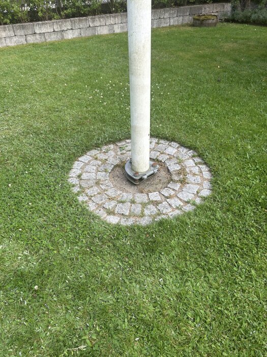 Stolpe omgiven av kullersten i en gräsmatta.