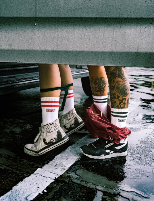 Två par ben med liknande strumpor och sneakers, en av personerna har synliga tatueringar.