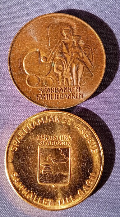 Två medaljer från Eskilstuna Sparbank, en med "Sparbanken Familjebanken" och en med "Eskilstuna Sparbank" och texten "Samhället till gagn".