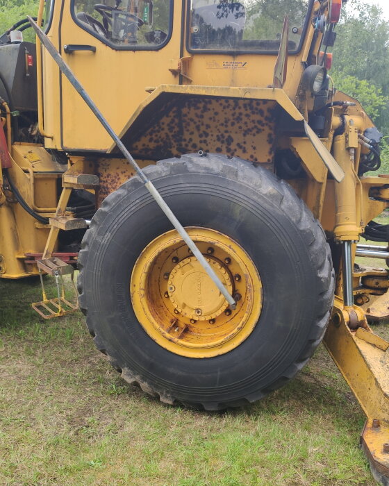 Gult traktordäck med en stor hävarm fastkilad för att ta loss muttrarna. Bakgrund av grönska och traktorens hytt synlig.