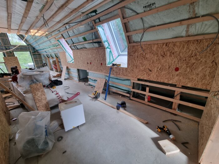 Renoveringsrum med träpanel och isolering på väggarna, verktyg och material spridda över golvet.