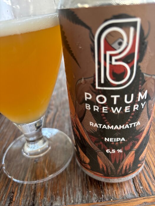 Flaska med etiketten "Potum Brewery Ratamahatta NEIPA 6,5%" och ett glas gyllene öl på träbord.
