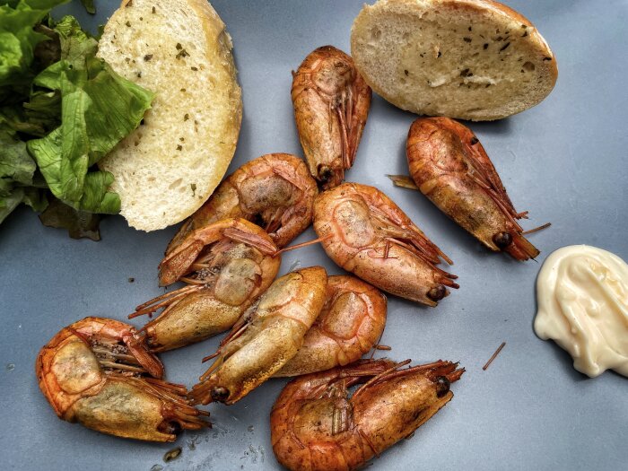 Rökta räkor på en tallrik med vitlöksbröd, sallad och aioli.