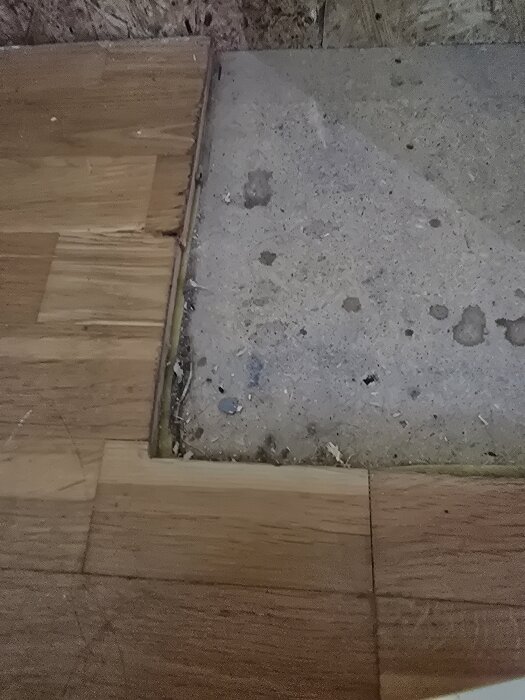Trägolv möter oregelbundet betongunderlag i hörn, med förberedda sågade kanter.