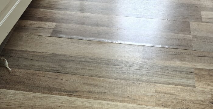 Golvplanka som har rest sig och bubblat i en skarv, troligen på grund av vattenläckage under diskmaskinen.