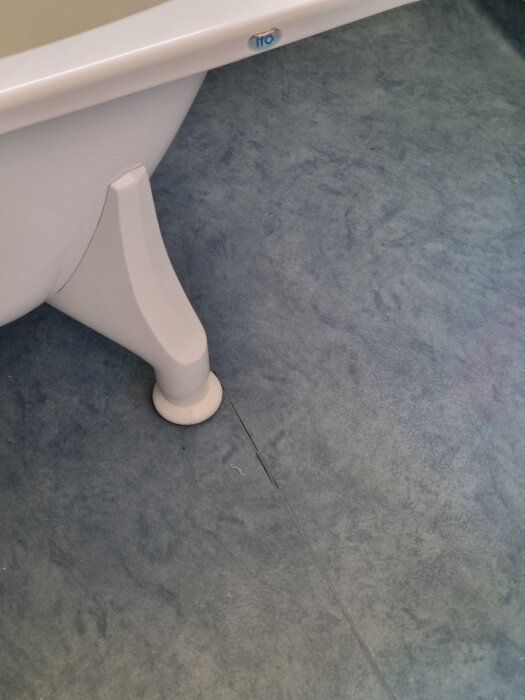 Badrumsmatta med spricka bredvid ett badkarsben.