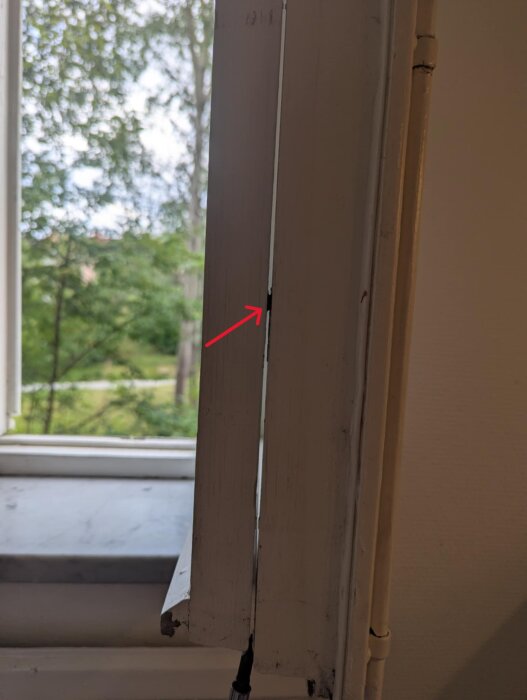 Inzoomad bild av ett fönster från sidan med en synlig skruv och hylsa mellan fönsterbågarna, samt en pil som visar dem.