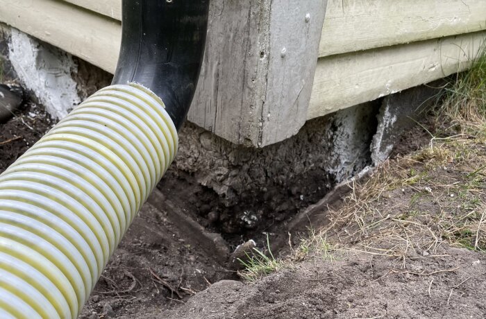 Glipa mellan betong och utsida av husgrund, med avloppsrör i förgrunden och gräsmatta runtom.