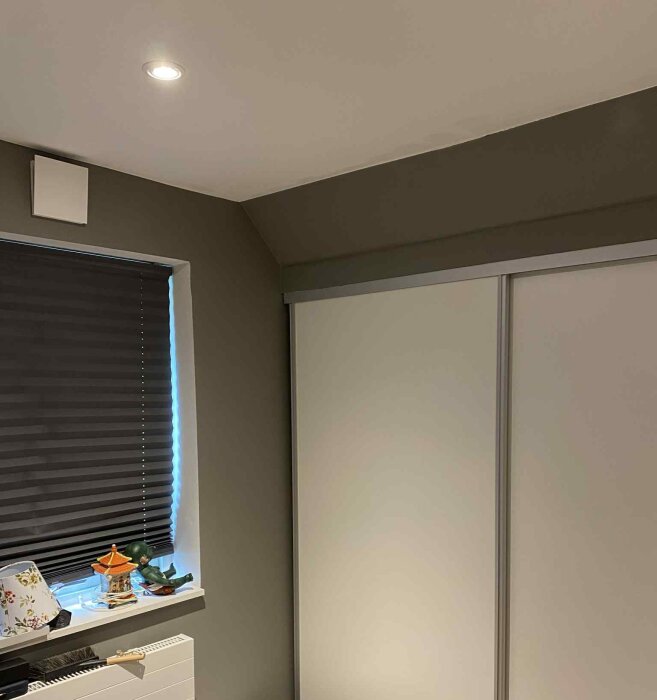 Sovrumshörn med snedtak, fönster med mörkläggningsgardin, och skjutdörrar till garderob.