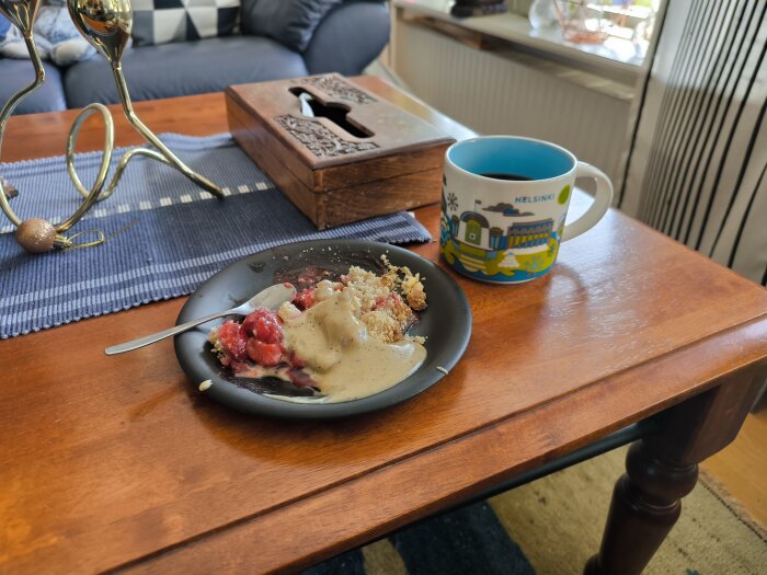 Jordgubbspaj med hemlagad vaniljsås på ett svart fat på ett bord, bredvid en mugg med texten "Helsinki".