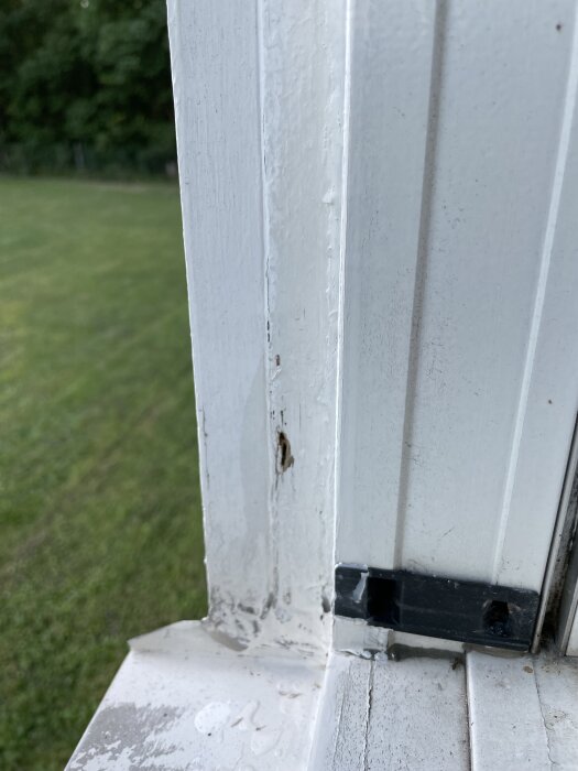 Rötskadat fönsterfoder med sprucken färg och skador, där träet separerar och visar tecken på slitage mellan två delar av fodret.