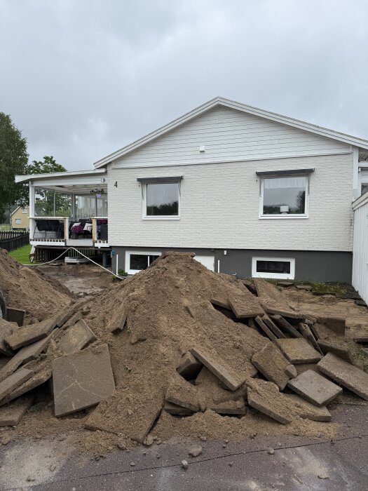 Grävd uppfart med borttagna markplattor och jordhögar framför ett hus.