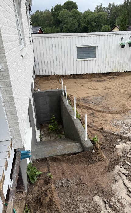 Grävd uppfart med borttagna markplattor, delvis synlig trappa och vit byggnad i bakgrunden. Området är klart för nästa byggsteg.
