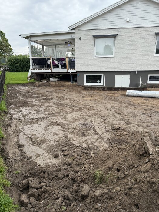 Uppfart grävd till rätt nivå, med jord och borttagen gräsmatta framför ett hus med altan. Grävyta uppskattad till 350-400 mm djup.