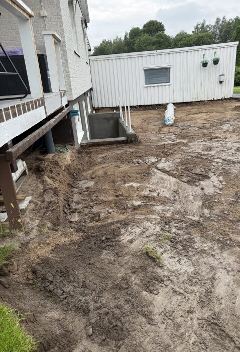 Uppgrävd uppfart med synlig jord och borttagna markplattor framför ett hus, redo för nästa byggsteg.