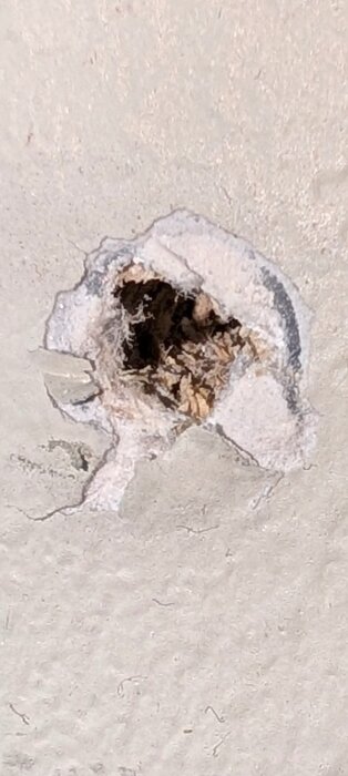 Inzoomad bild av ett borrhål i en innervägg, med synligt material som ser ut som träspån och gips.