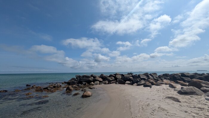Klippor och sandstrand vid havet under molnig himmel i Skagen.