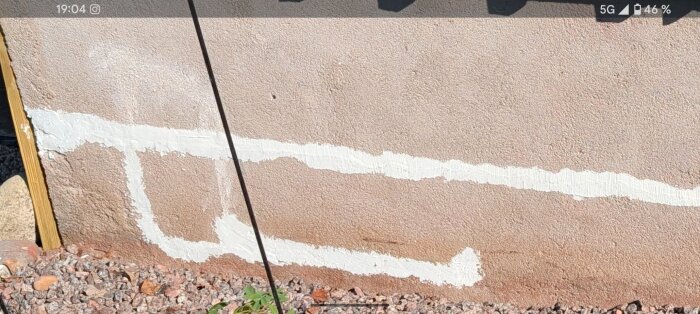 Sprickor i en betongplatta täckta med ljust husfix ovanpå mörkare grund, med stenar vid kanten.