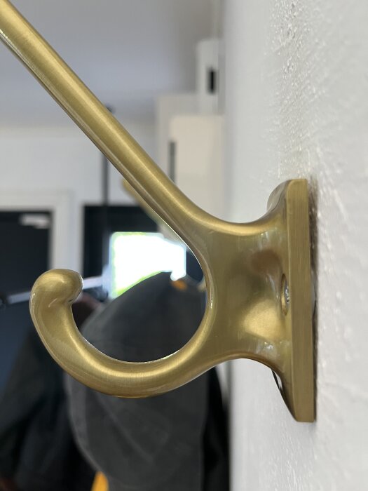 Väggmonterad krok i gyllene metall fixeras i gipsskiva, bilden visar problem med lösning där kroken gungar och sitter löst.