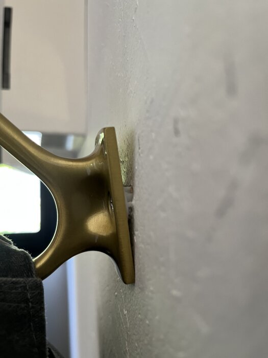 Guldfärgad krok som lossnar från en vit vägg, del av ett projekt där upphängningen inte sitter stadigt i gipsvägg.