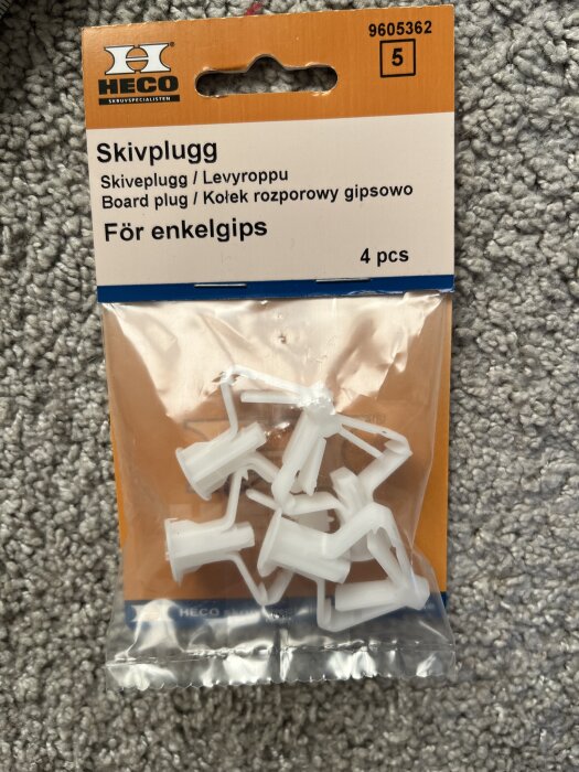 Förpackning med fyra vita skivpluggar för enkelgips från märket HECO, ligger på en grå matta.