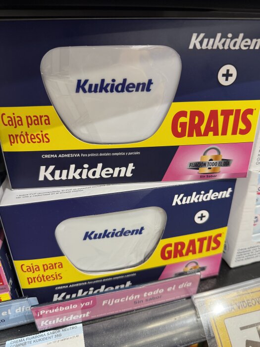Förpackning med Kukident tandproteslim, märkt som gratis, placerad på en hylla i en butik.