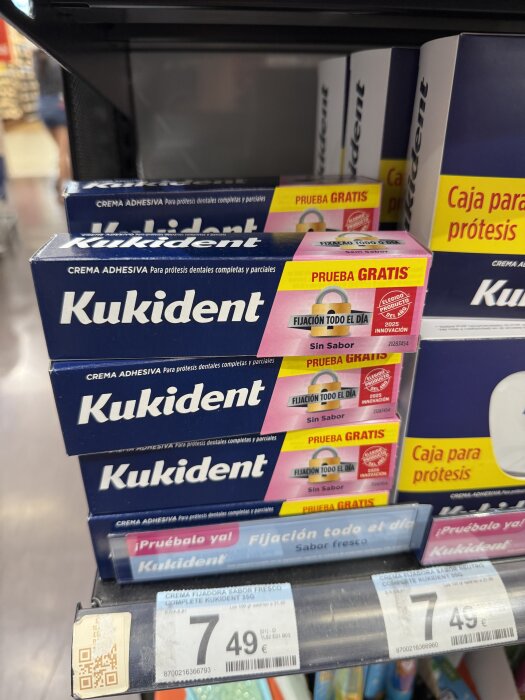 Förpackningar av Kukident tandproteslim med texten "Prueba Gratis" och "Sin Sabor" i en butikshylla.