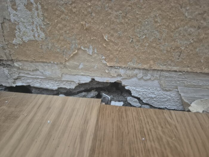 Spricka i betongvägg vid golvsockel med flagnande tapet och synlig skada.
