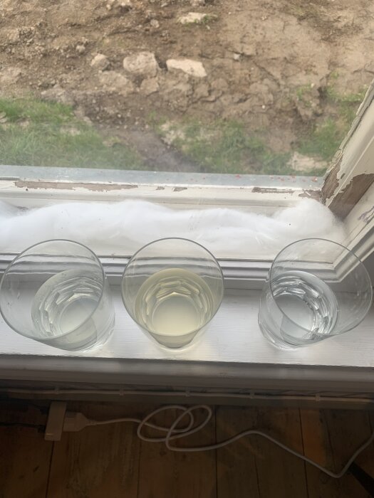 Tre glas vatten på en fönsterbräda: första från en brunn idag, andra taget en vecka efter renovering, tredje glaset innehåller klart kommunalt vatten.