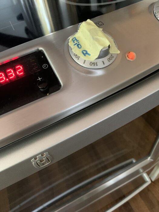 Ugnens termostat i närbild med en gul tejpbit markerad 200 grader och ett rött lysande ljus bredvid på kontrollpanelen.