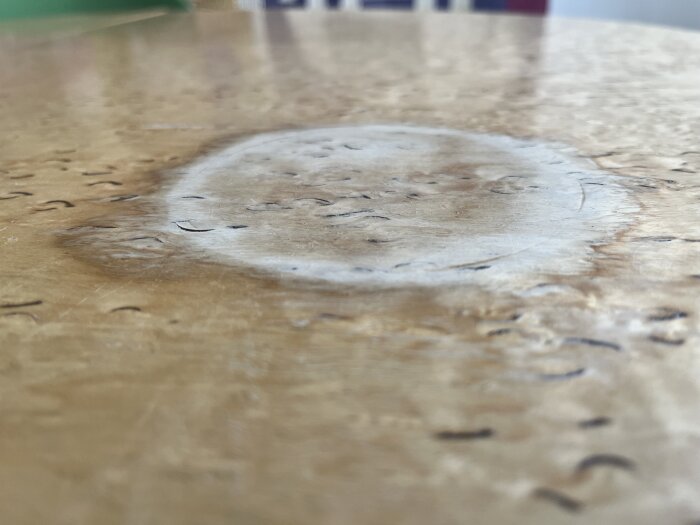 Närbild på ett träbord med en stor vit ring och skador på ytan.