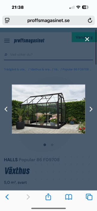 Svart växthus på 5 m² med glasväggar, inrett med bord och stolar samt omgivande växter och häck i bakgrunden.