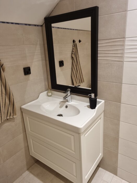 Badrum med nyupphängd spegel över ett tvättställ och nyinstallerad kran; handduk och tvålpump synliga.